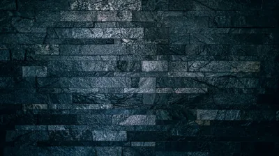 Rough slate strips stack across the wall in cold blue-grey, the light pooling near the centre and the corners sunk in shadow.