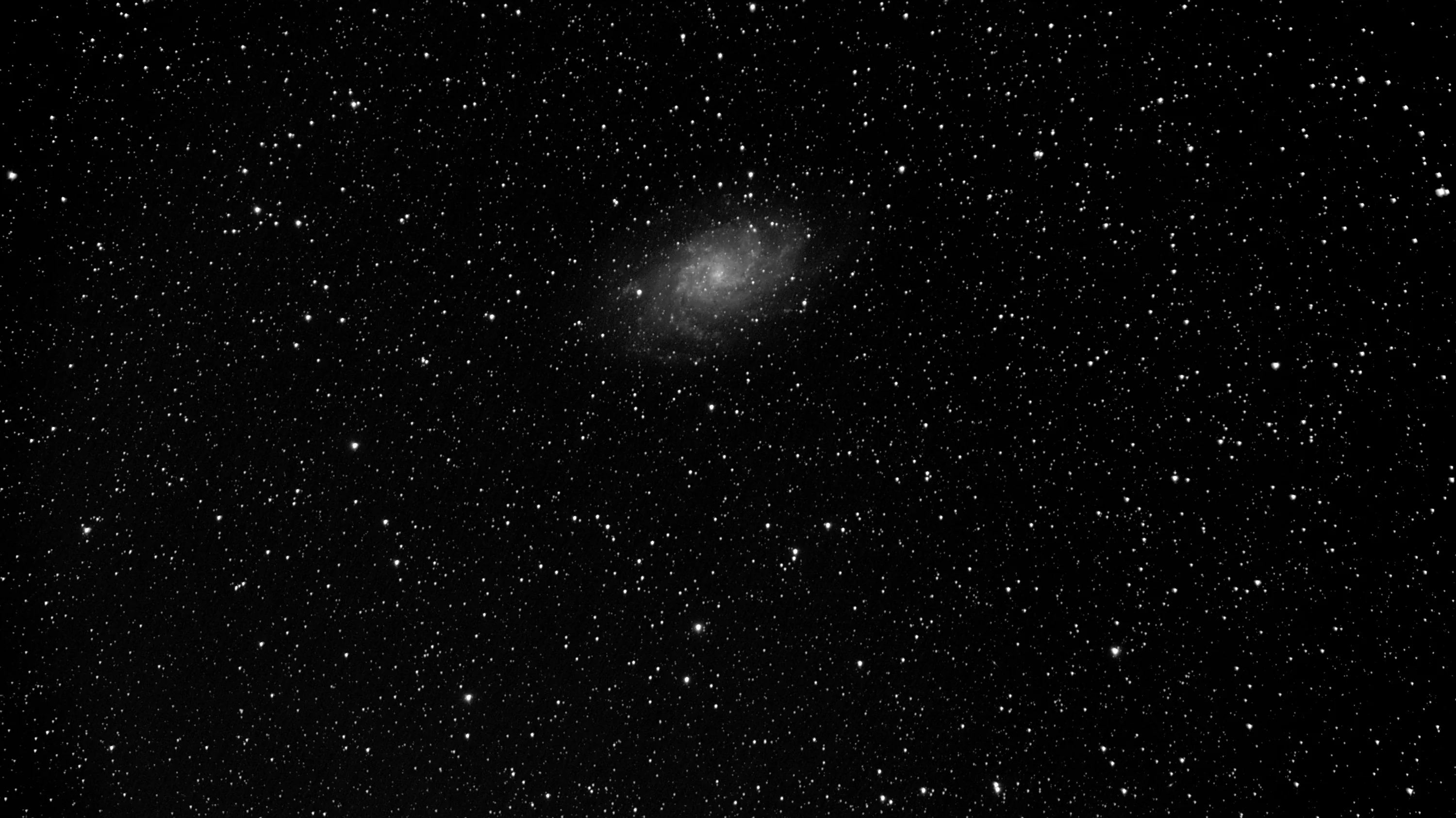 A faint spiral galaxy sits just above centre in a thick monochrome star field, its arms barely brighter than the stars around it.