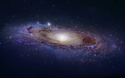 The Andromeda galaxy tilts across the centre with a bright cream core, fine stars dusting the black around it; both lower corners stay dark for desktop icons.