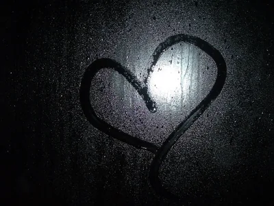 A finger-drawn heart on a misted window at night, one streetlight blurring through the condensation just inside the shape.