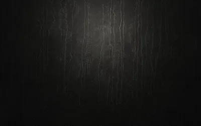 Vertical scratches and drip marks run down a matte black wall, caught by a dim light from above that leaves the lower corners in near total darkness.