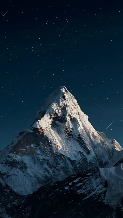 A sharp snow-covered peak rises into a star-filled night sky, moonlight catching the ridge on the left while the base stays in shadow.