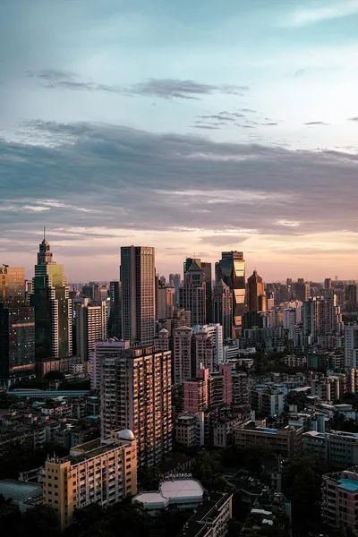 Downtown towers catch the last warm light of the day under a pale blue sky, dense rooftops filling the lower half of the frame.