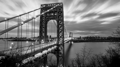 A long-exposure shot of a suspension bridge in monochrome, streaked cloud overhead and headlights blurred on the deck.