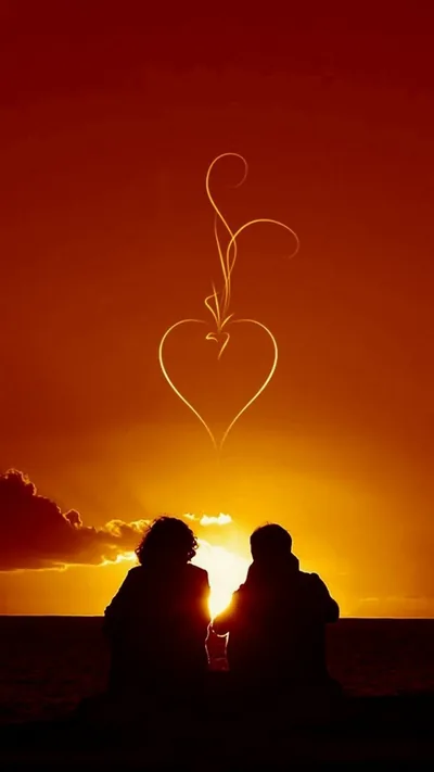 A couple sit on a low wall watching an orange sunset, a heart traced in thin white light hanging above the clouds.