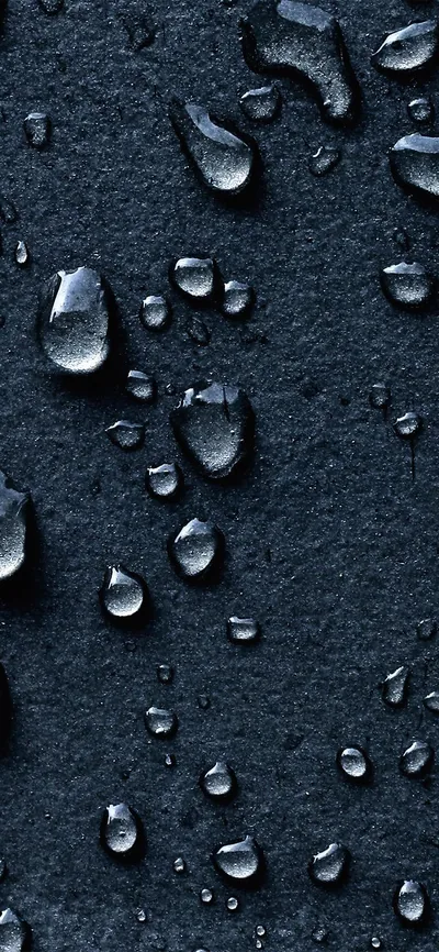 Beads of water sit scattered across a rough dark slate surface, each one catching a small cold highlight along its upper edge.