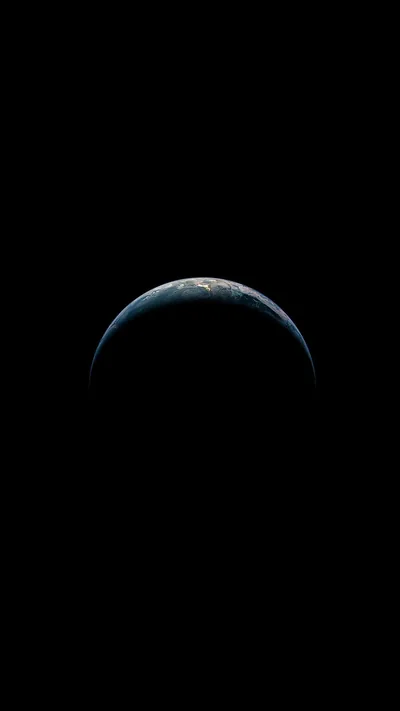 A thin lit crescent curves along the top of the planet with cloud detail just visible, the rest of the globe lost in shadow.