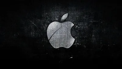 The bitten-apple mark sits centre-left on a scuffed dark canvas, its surface picking up the same scratches and stains as the wall behind it.