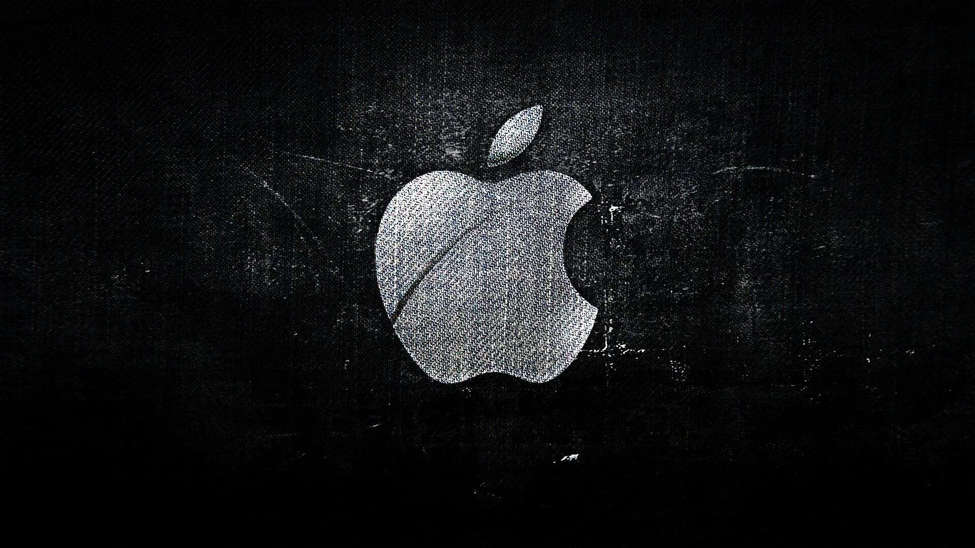 The bitten-apple mark sits centre-left on a scuffed dark canvas, its surface picking up the same scratches and stains as the wall behind it.