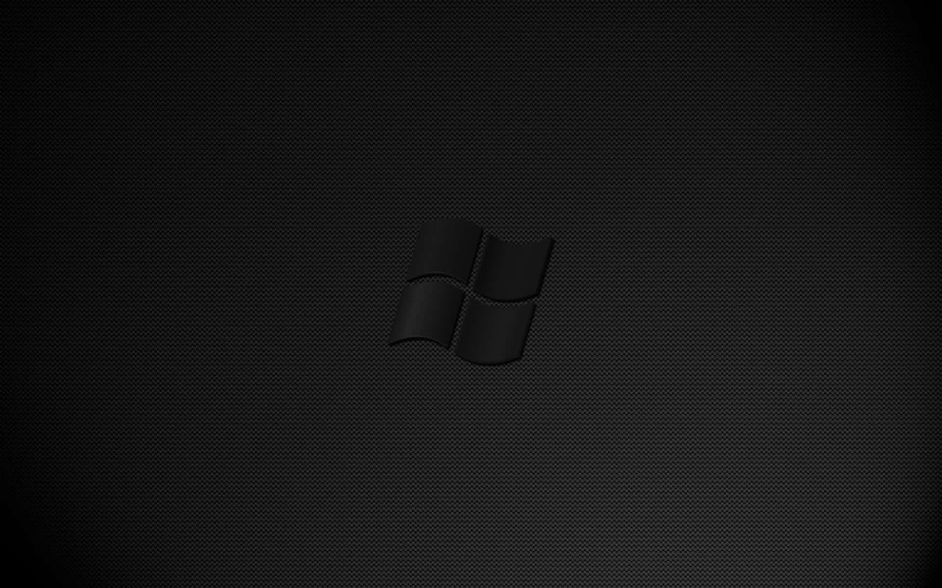 The Windows flag is pressed into a finely ridged charcoal surface, lit from above so only the edges of the emblem catch light.