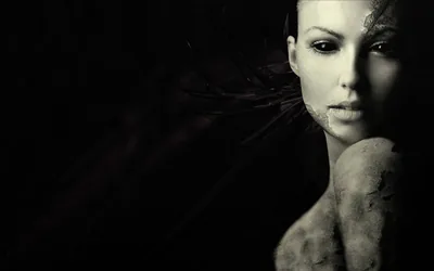 Cracked-glass textures break across a pale face and shoulder on the right, dark eyes catching faint light, while the left half of the frame stays pure black.