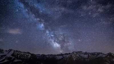 The bright core of the Milky Way tilts over snow-dusted peaks, its dust lanes sharp against a violet-blue starfield.