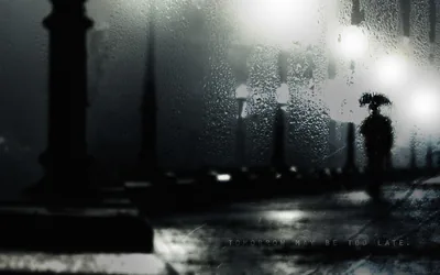 Rain beads on the glass blur an umbrella carrier and a row of glowing street lamps, the left third of the frame dropping into deep black.