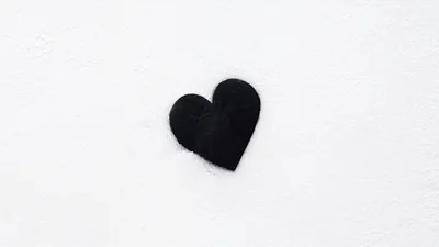 A small hand-painted black heart sits just left of centre on rough white plaster, the rest of the wall left plain and evenly lit.
