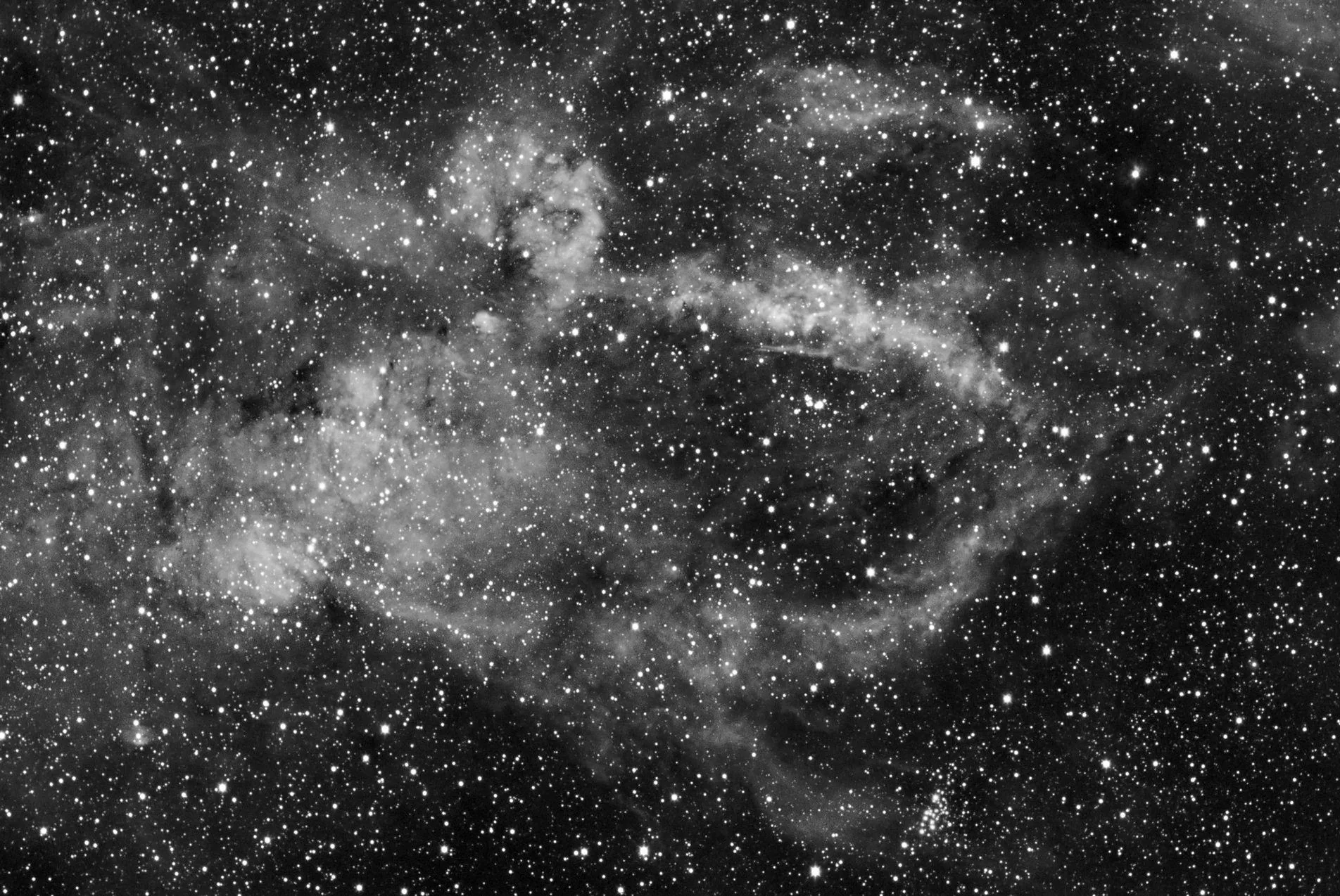Faint monochrome nebulosity drifts through a dense field of white stars, the gas showing only as soft grey wisps against black.