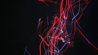 Tangled red and white light trails twist in the centre of a near-black frame, caught by moving the camera during a long exposure.