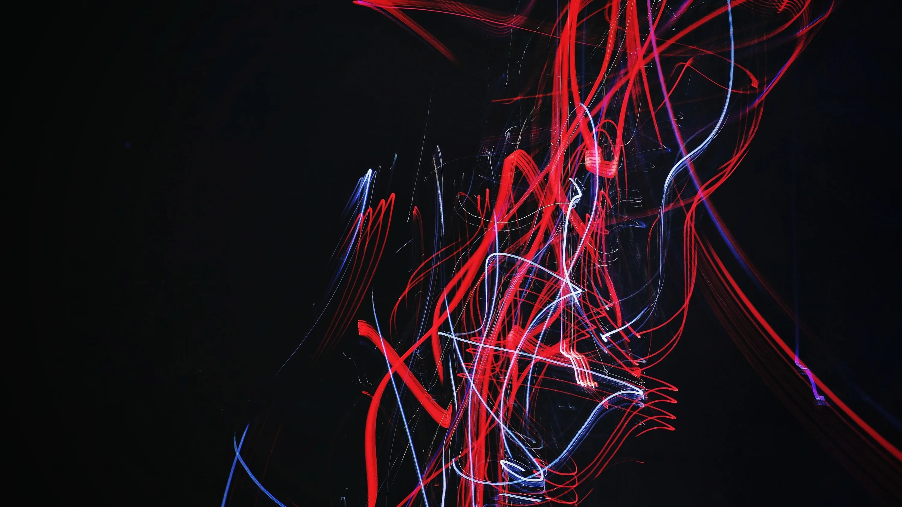 Tangled red and white light trails twist in the centre of a near-black frame, caught by moving the camera during a long exposure.