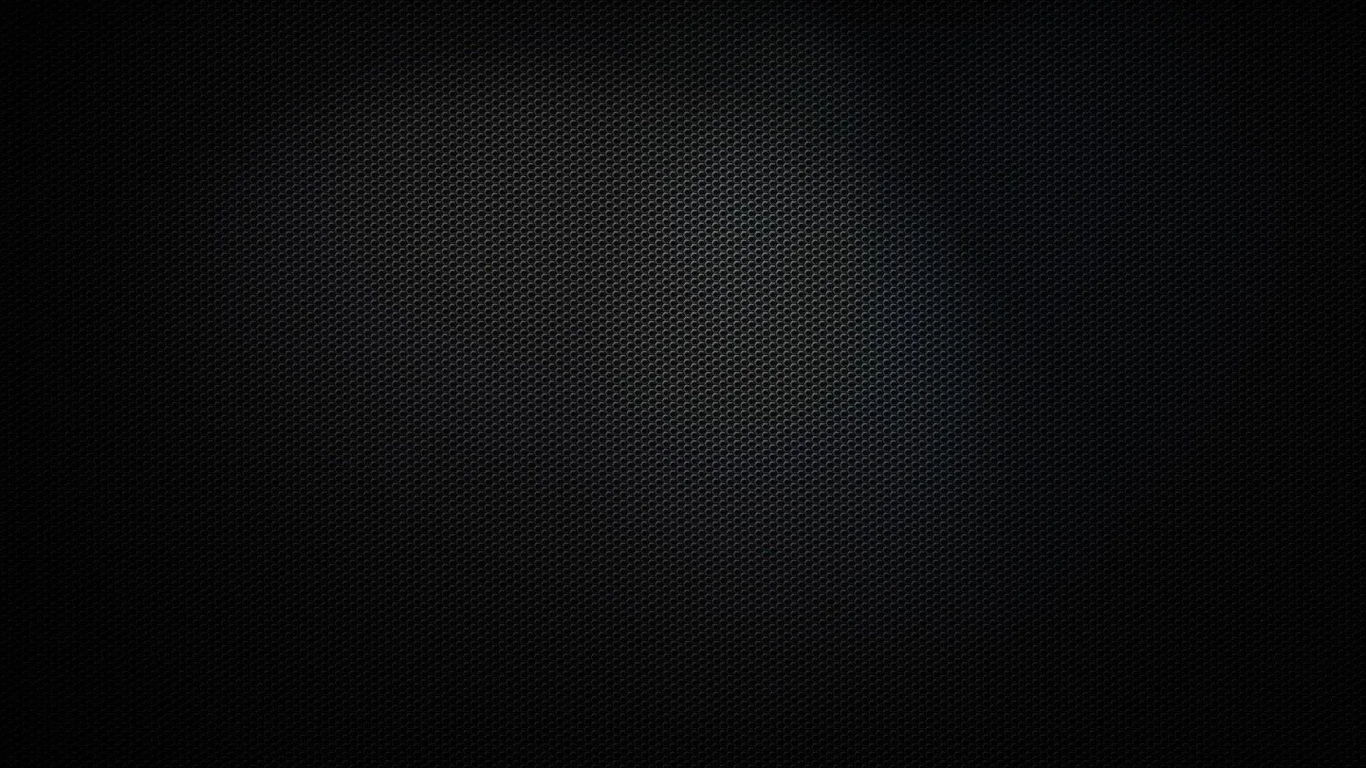 A tight carbon mesh weave covers the whole surface, a faint pool of light at the centre and the border sinking to black.
