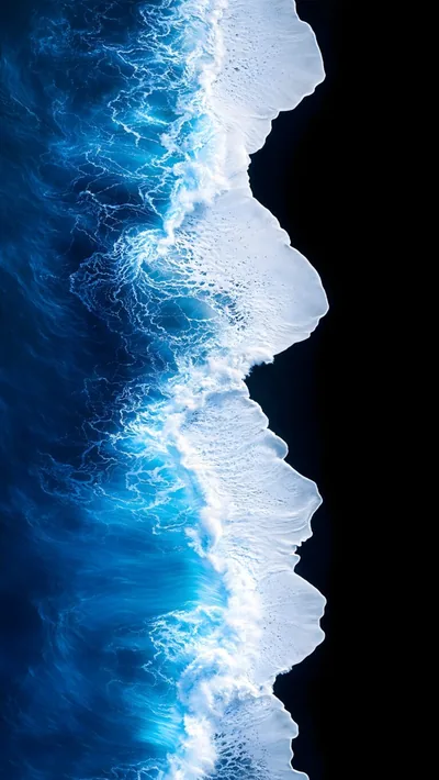 Shot from directly above, white foam breaks in a ragged line where turquoise water meets a beach of near-black volcanic sand.