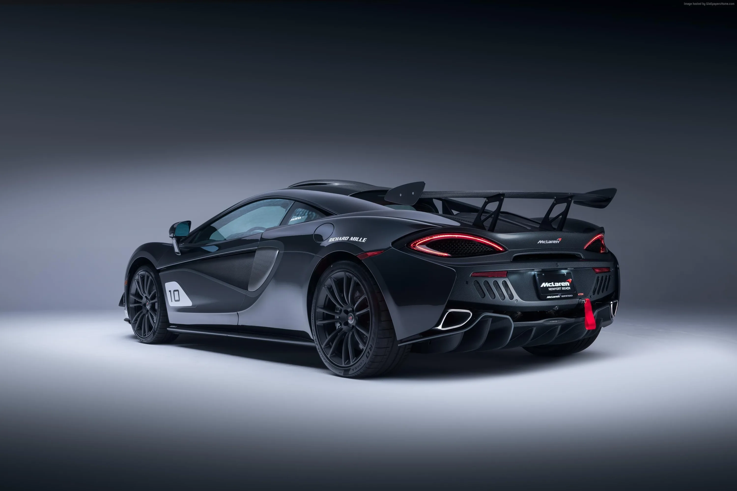A black McLaren with a tall track wing photographed against a soft grey backdrop, red brake calipers and a small flash of pink trim the only colour.