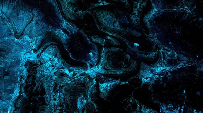 Wet rock ledges photographed from above, every ridge outlined in cold teal while the hollows stay black.