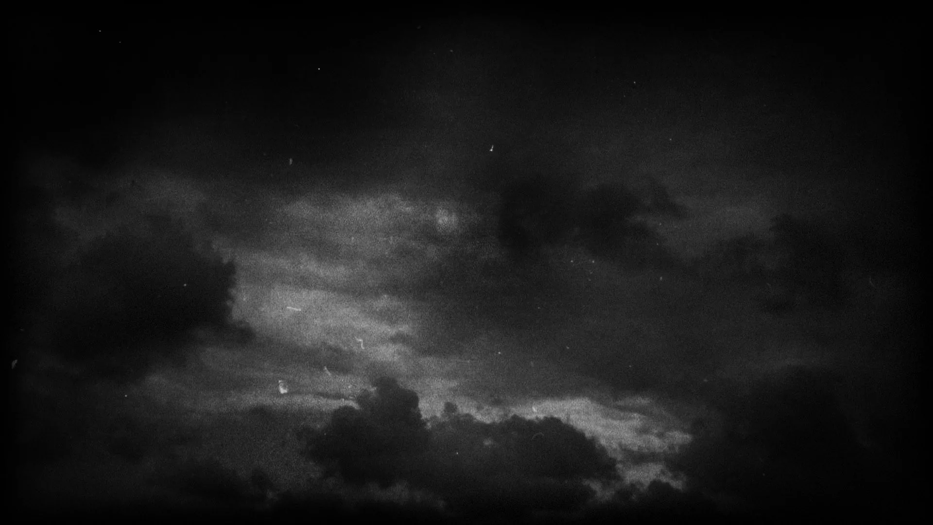 Heavy clouds break apart across a grainy night sky, a few stars showing through the gaps while the bottom edge sinks to near black.