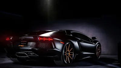 Rear three-quarter of an Aventador in an unlit studio, the Y-shaped tail lamps and a hot exhaust glow burning red while bronze rims catch a thin edge of light.