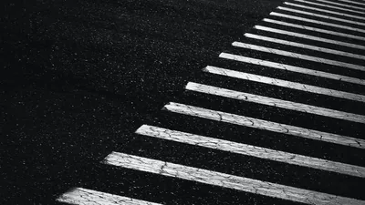 White zebra stripes cut diagonally across coarse black asphalt in monochrome, the top left corner left entirely empty.
