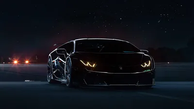 A wide-body Lamborghini faces the camera on an empty road at night, its angular headlights glowing amber while stars and distant orange lights fill the background.