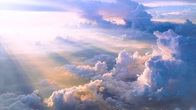 Crepuscular rays slant from the upper left across towering soft-blue clouds, the light landing warmest in the lower left of the frame.