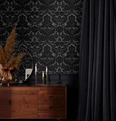 Textured damask wallpaper rises behind a mid-century walnut sideboard, a heavy black curtain closing off the right third of the frame.
