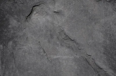 A slab of grey stone photographed flat, deep splits running diagonally from the top corner and the surface pitted where pieces have flaked off.