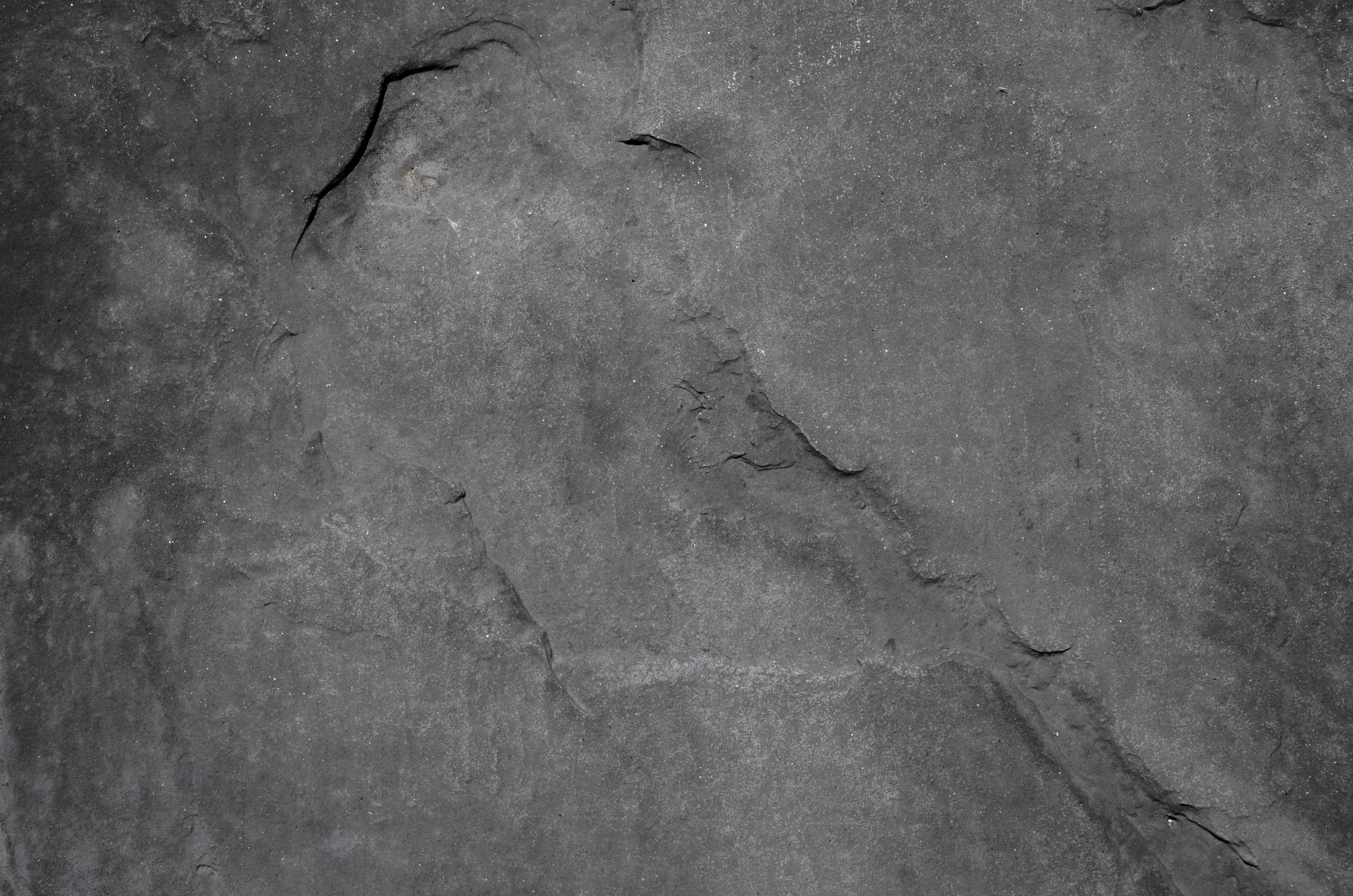 A slab of grey stone photographed flat, deep splits running diagonally from the top corner and the surface pitted where pieces have flaked off.