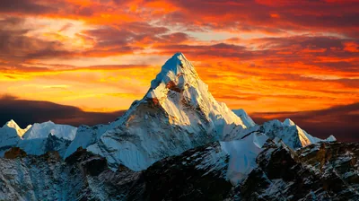 Golden evening light picks out a steep Himalayan snow face while red and orange clouds burn across the whole sky behind it.