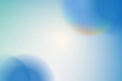 Two out-of-focus blue discs sit in opposite corners of a pale sky-white field, with a faint warm glint on the upper one.