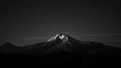 A snow-streaked summit and a smaller peak beside it catch the last light in black and white, the sky and lower slopes sinking into shadow.