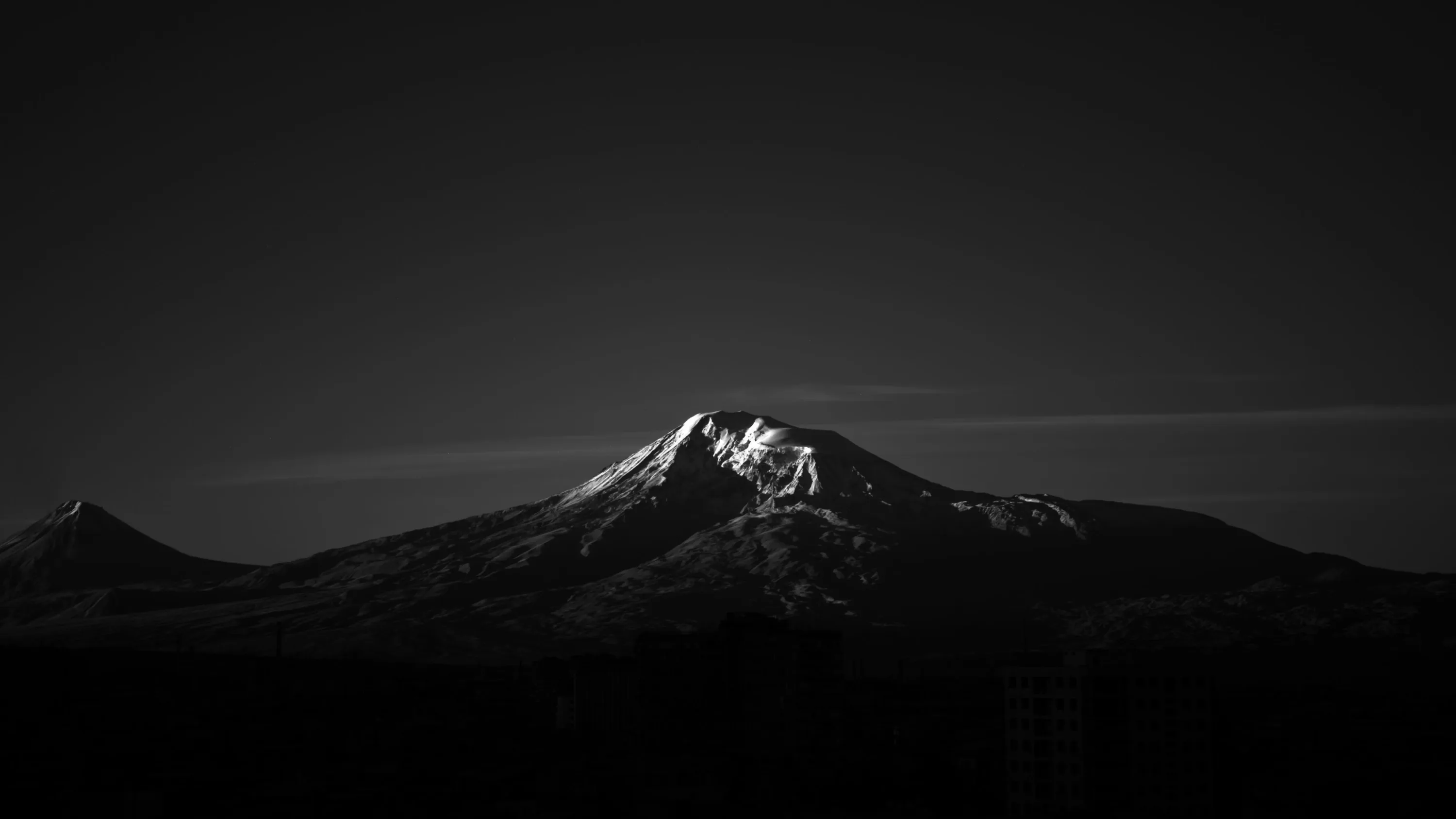 A snow-streaked summit and a smaller peak beside it catch the last light in black and white, the sky and lower slopes sinking into shadow.