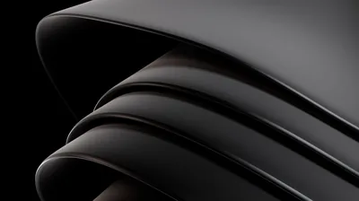 Layers of a smooth dark material peel back from one another, the topmost fold catching a soft rim of light.