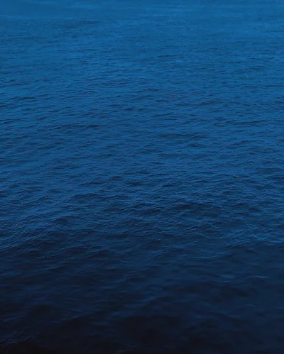 A calm sheet of navy sea fills the tall frame with barely a ripple, slightly lighter at the top and shading darker toward the bottom edge.