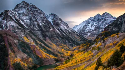 The twin Maroon Bells stand snow-dusted over a valley of turning aspens, muted evening light holding the scene in soft greys and golds.