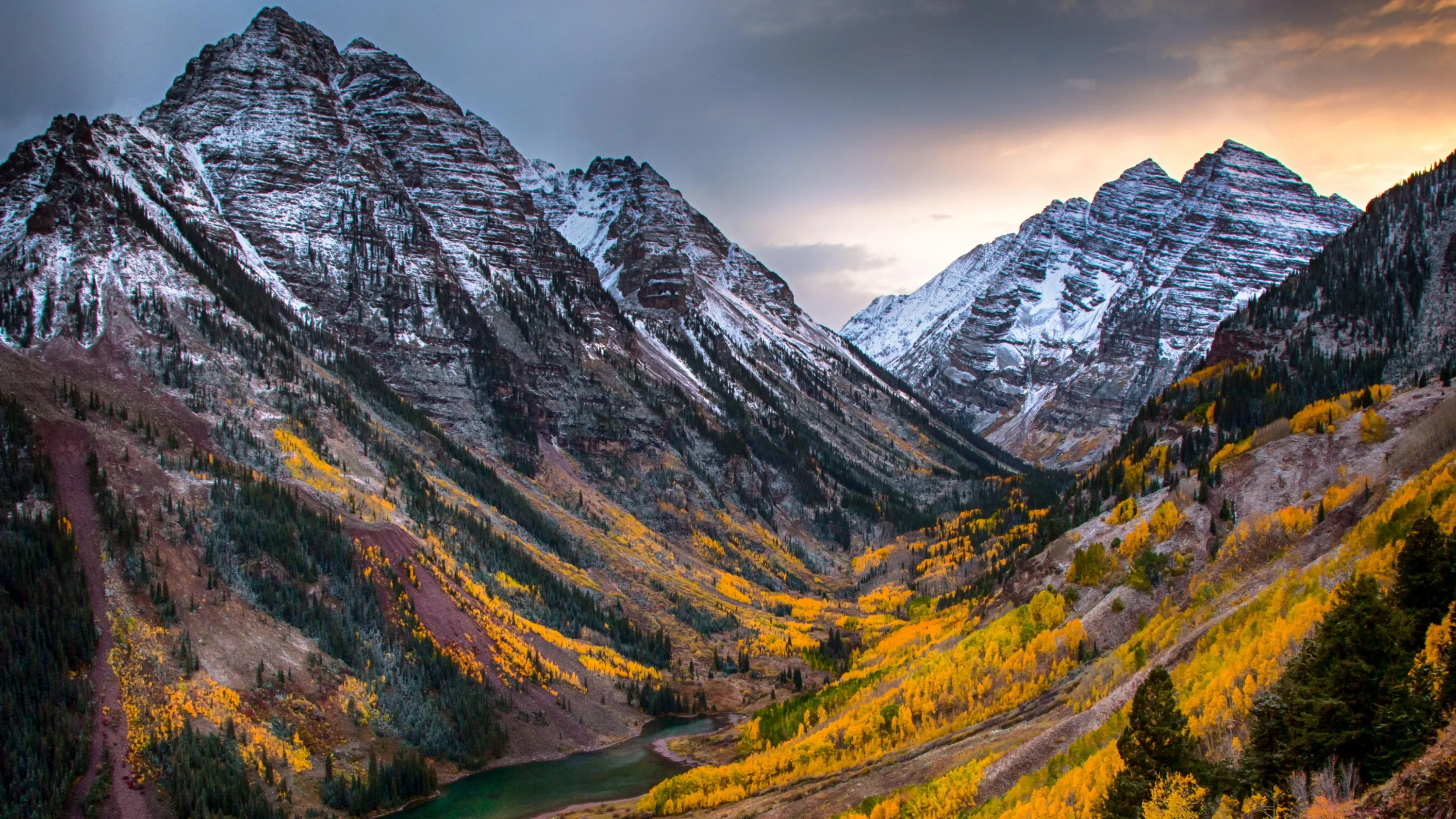 The twin Maroon Bells stand snow-dusted over a valley of turning aspens, muted evening light holding the scene in soft greys and golds.