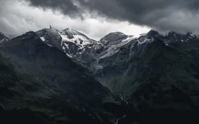 Heavy grey cloud presses down on glaciated summits, the valleys falling away into near-black shadow that hides desktop clutter.