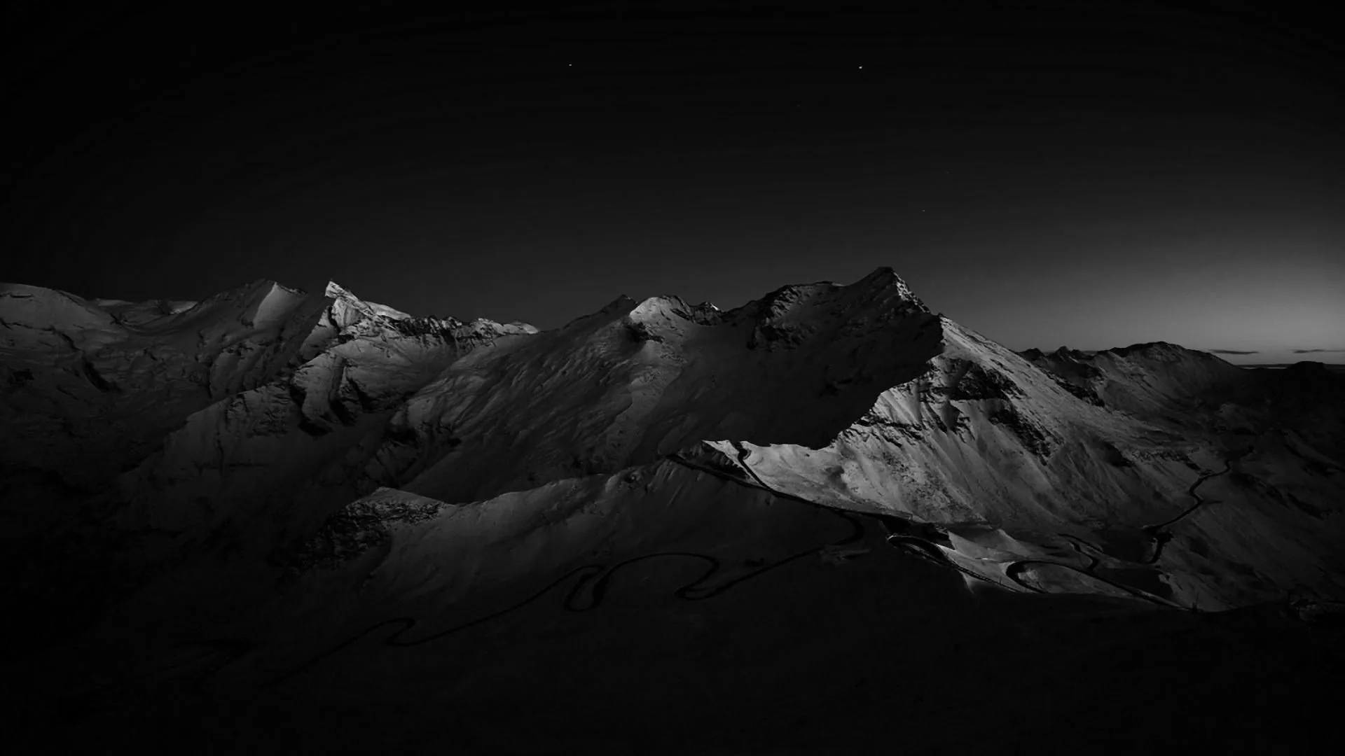 A jagged snowy ridge runs across the middle of the frame, faint stars overhead and a cold glow lingering on the right horizon.