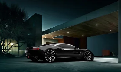 A long-tailed black coupe rests under a modern concrete carport in blue evening light, warm glow spilling from the house wall behind it.