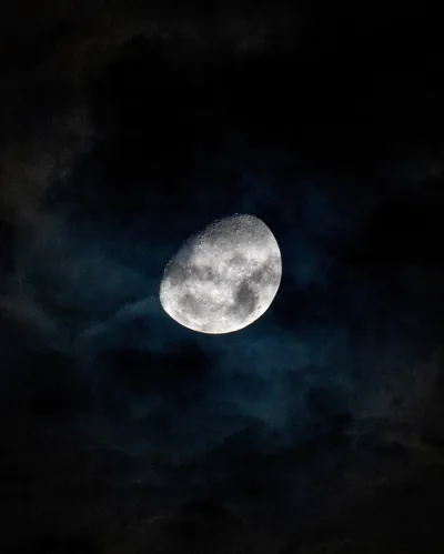 Thin blue-grey clouds drift across a bright gibbous moon, the corners falling to full black — a moody frame for an OLED lock screen.