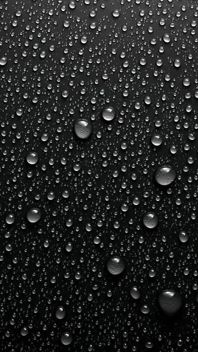 Beads of water sit across a dark grey panel, the larger ones near the bottom holding a bright pinpoint where the light comes in from the left.