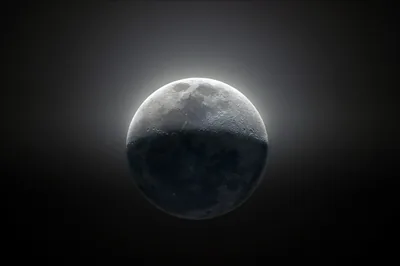 Light blazes along the moon's upper rim while its lower half sinks into shadow, the rest of the frame flat black for OLED screens.