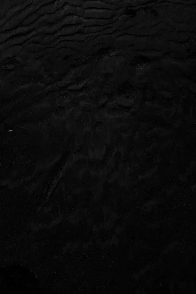 Shallow ripples cross a matte black surface in a tall frame, showing up only as slight shifts in shading.