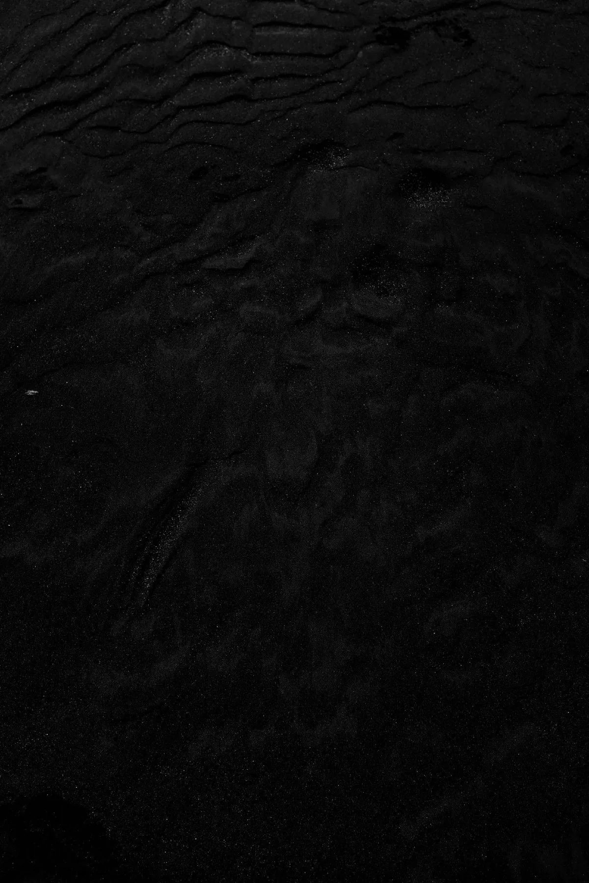 Shallow ripples cross a matte black surface in a tall frame, showing up only as slight shifts in shading.
