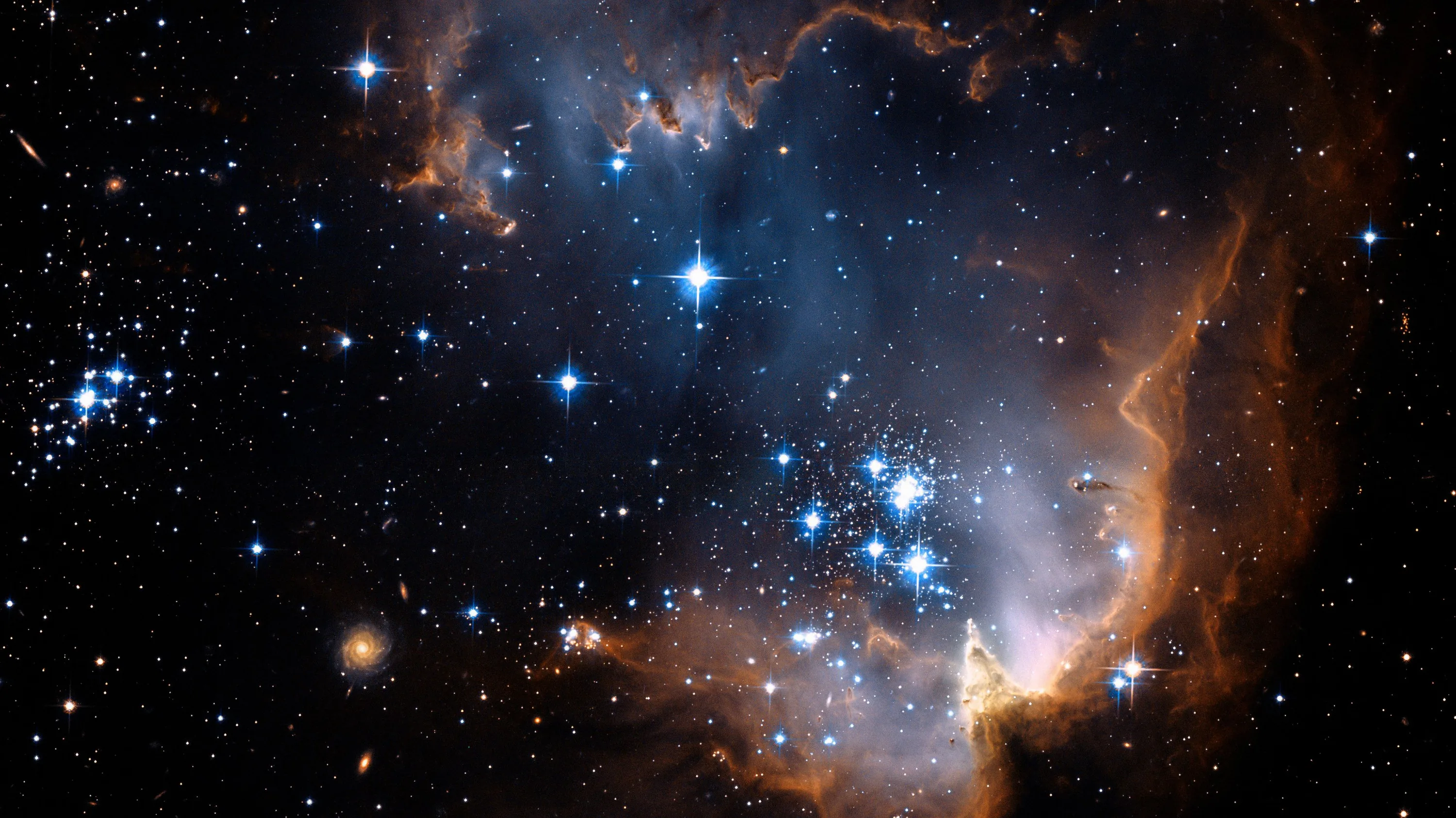 Bright blue newborn stars cluster mid frame while amber dust ridges arc along the top and right, a small galaxy visible near the lower left.